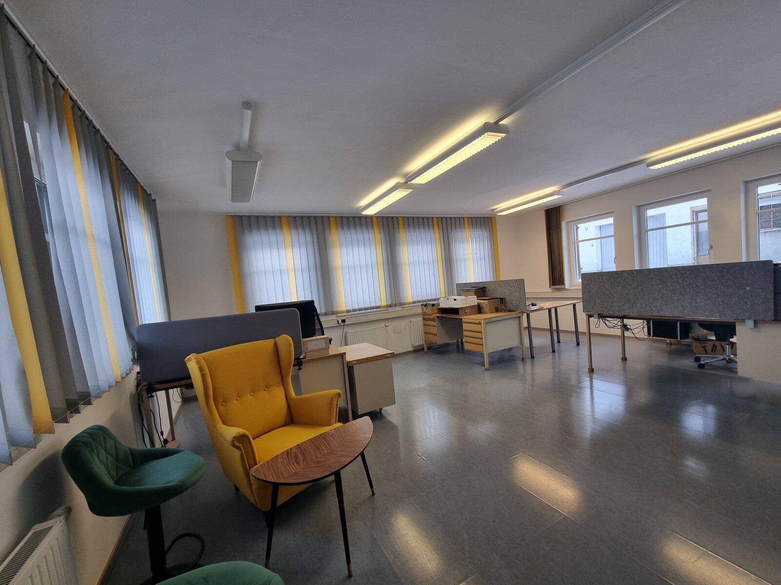Großes Büro mit mehreren Arbeitsplätzen, gelben Akzenten und Vinylboden.