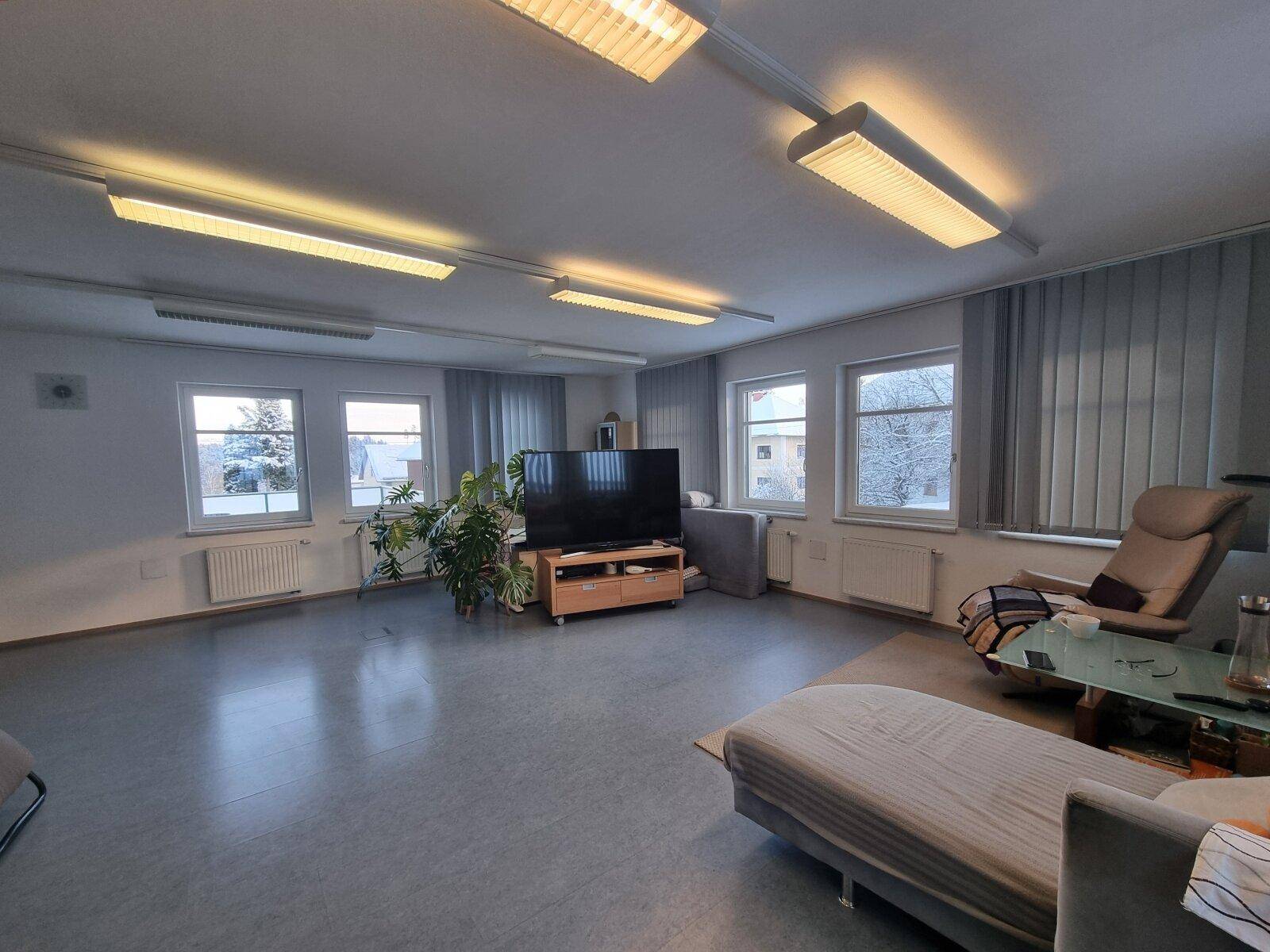 Heller Wohnraum mit großem Fernseher, Pflanzen und Blick auf die verschneite Landschaft.