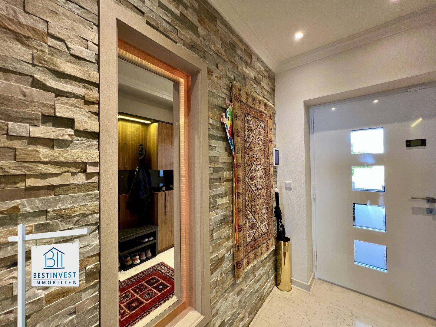 Heller Eingangsbereich mit Natursteinwand und moderner Haustür, die zu einem Holzschrank führt.