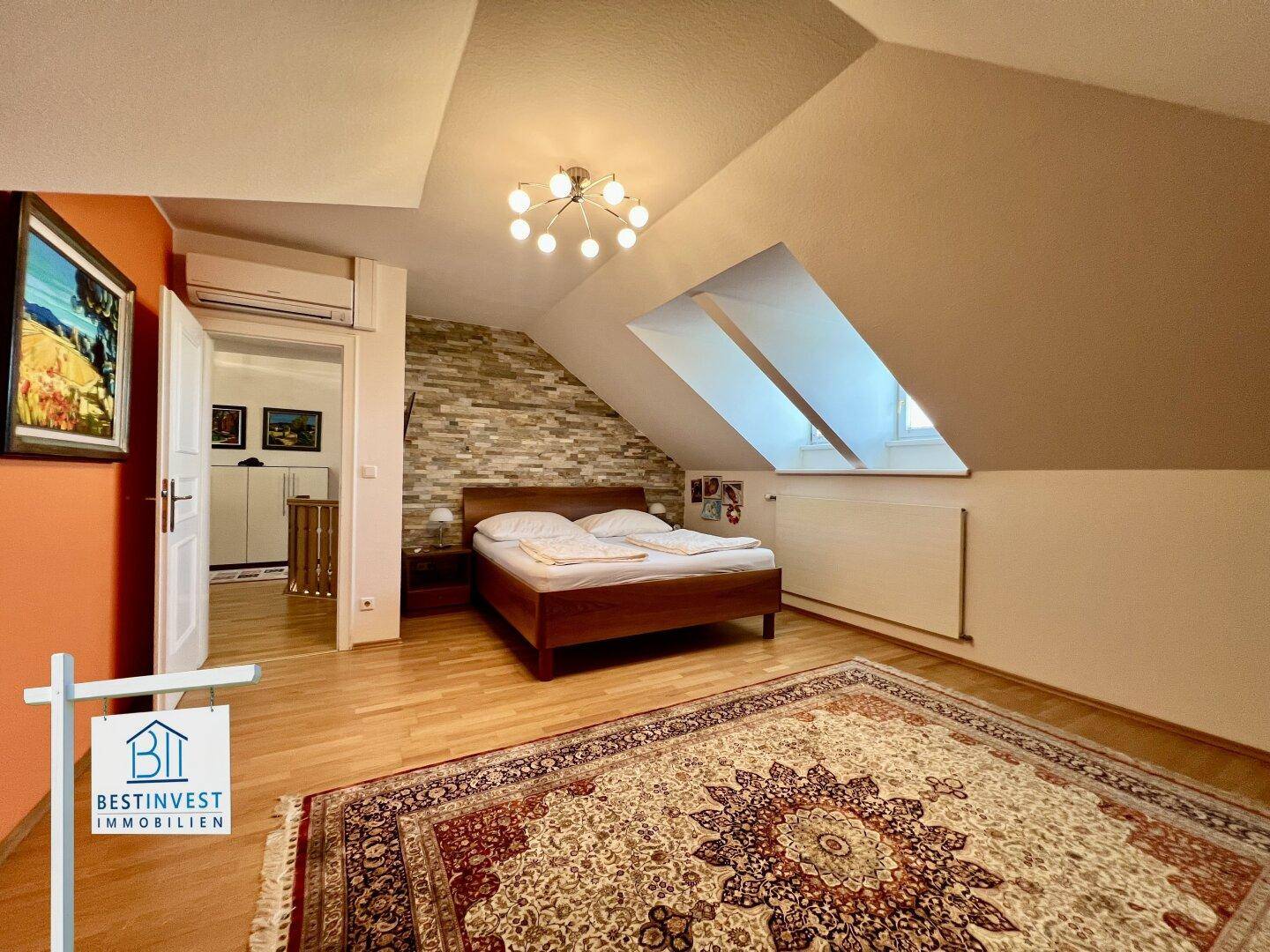 Schlafzimmer mit Dachschräge, Bett und dekorativer Steinwand, ausgestattet mit Klimaanlage.