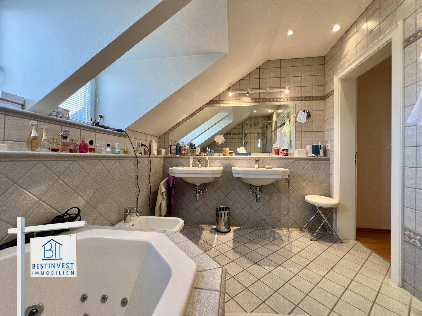 Geräumiges Badezimmer mit Eck-Whirlpool, Doppelwaschbecken, Bidet und Fliesen, unter Dachschräge.