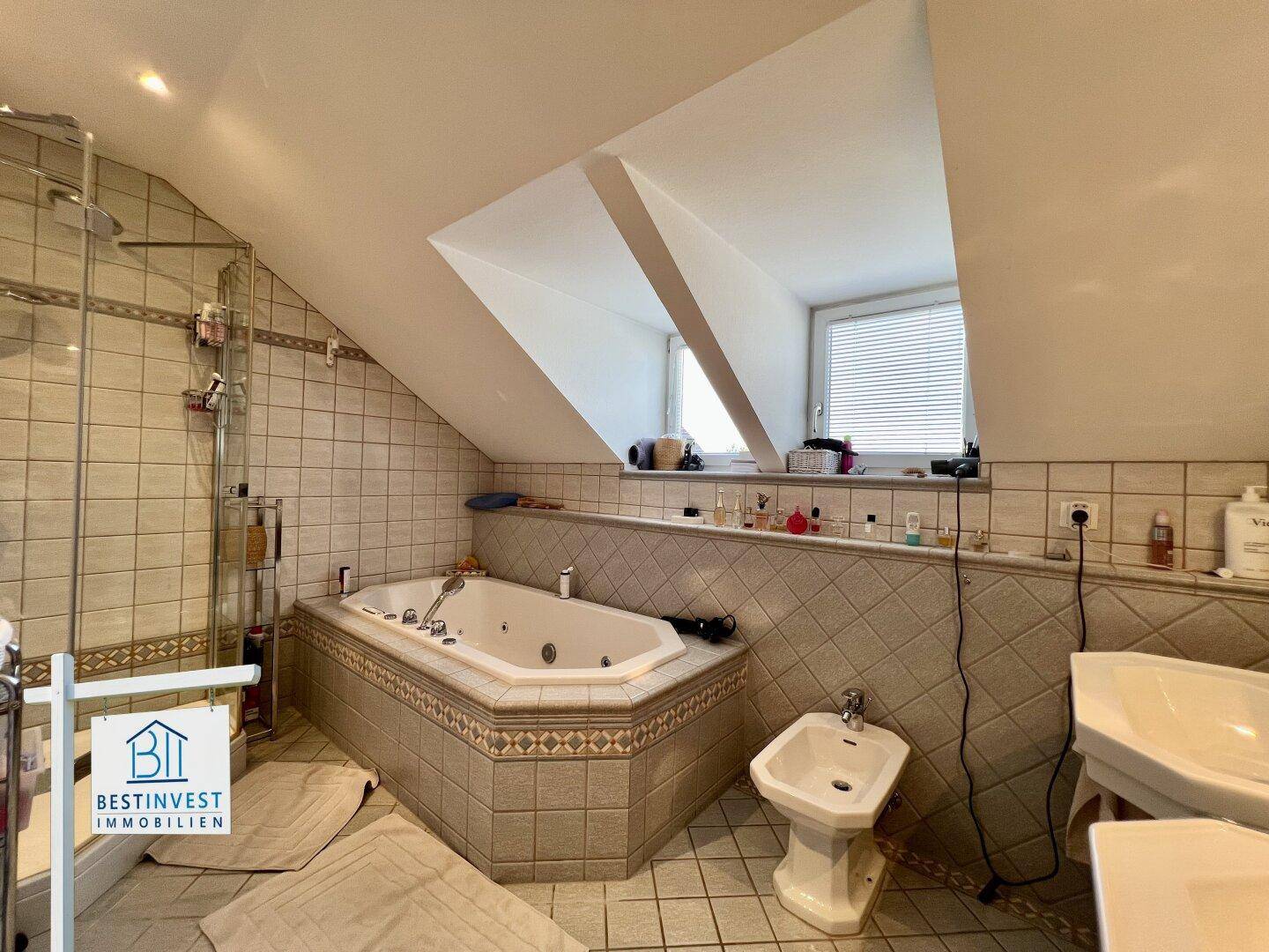 Badezimmer mit Duschbereich neben dem Whirlpool, Doppelwaschbecken und Bidet unter Dachschräge.