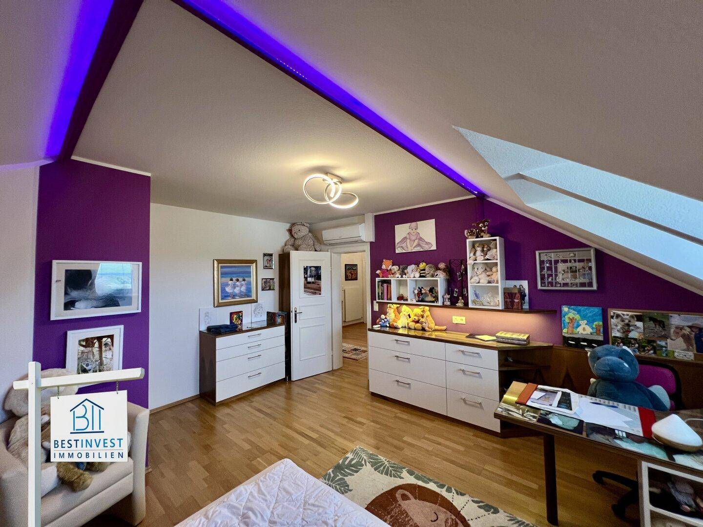 Kinderzimmer mit lila Wänden, Holzfußboden und Bett, beleuchtet durch dekorative Deckenleuchten.