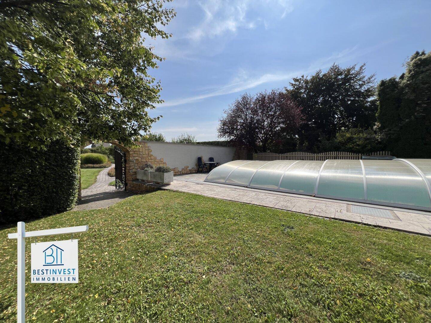Gepflegter Gartenbereich mit überdachtem Pool und Steinmauer im Hintergrund.