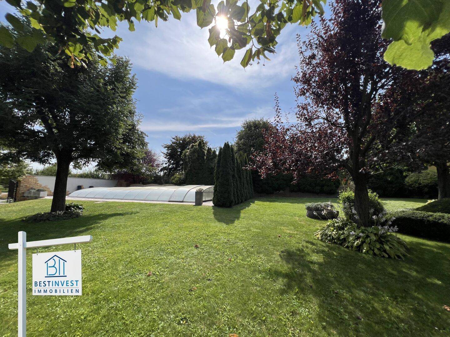 Großer Garten mit Rasenfläche, Bäumen und einem überdachten Swimmingpool.