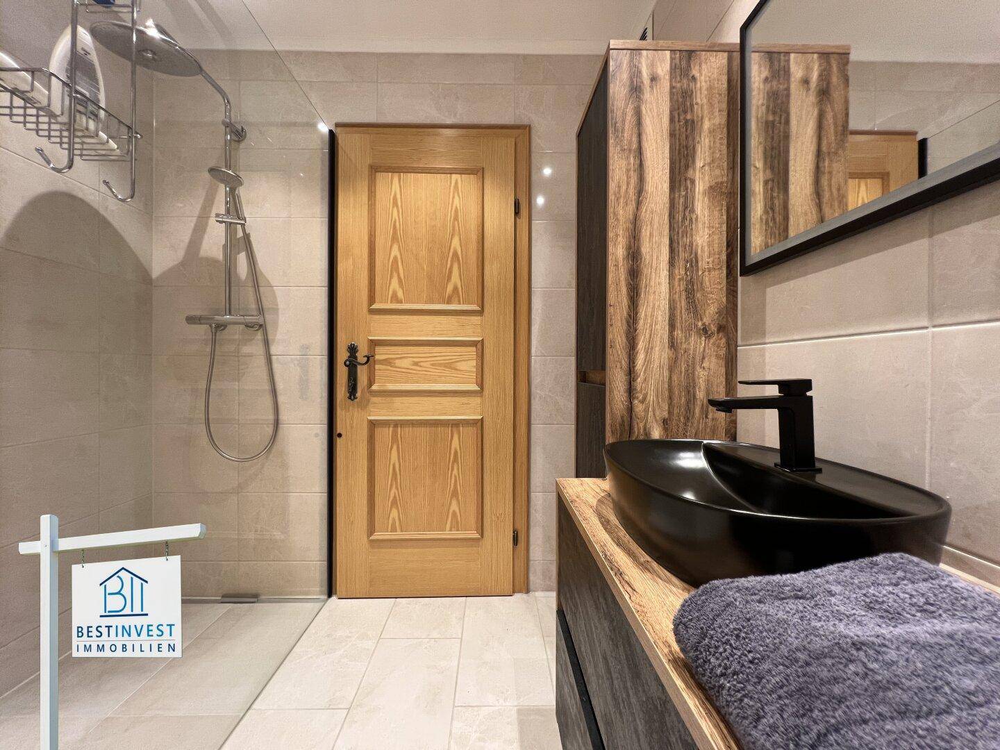 Modernes Badezimmer mit begehbarer Dusche, schwarzem Waschbecken und Holzschrank.