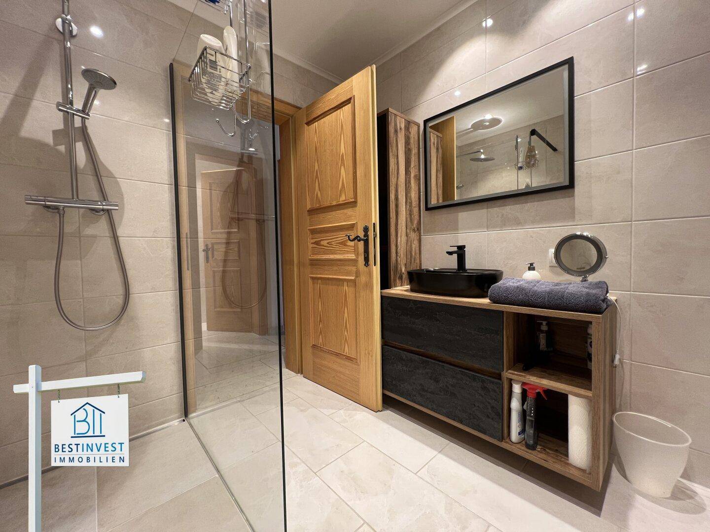 Modernes Badezimmer mit begehbarer Dusche, dunklem Waschbecken und Holzdetails.