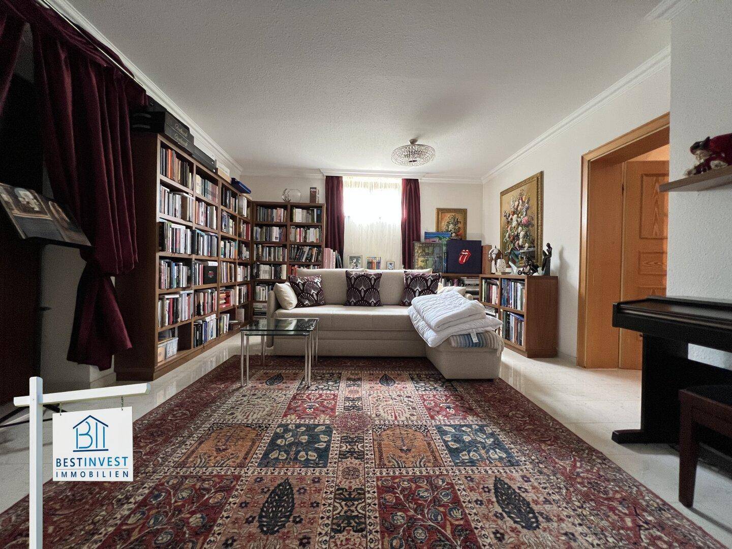 Gemütliches Wohnzimmer mit umfangreichen Bücherregalen, Sofa und Teppich, ideal zum Entspannen.
