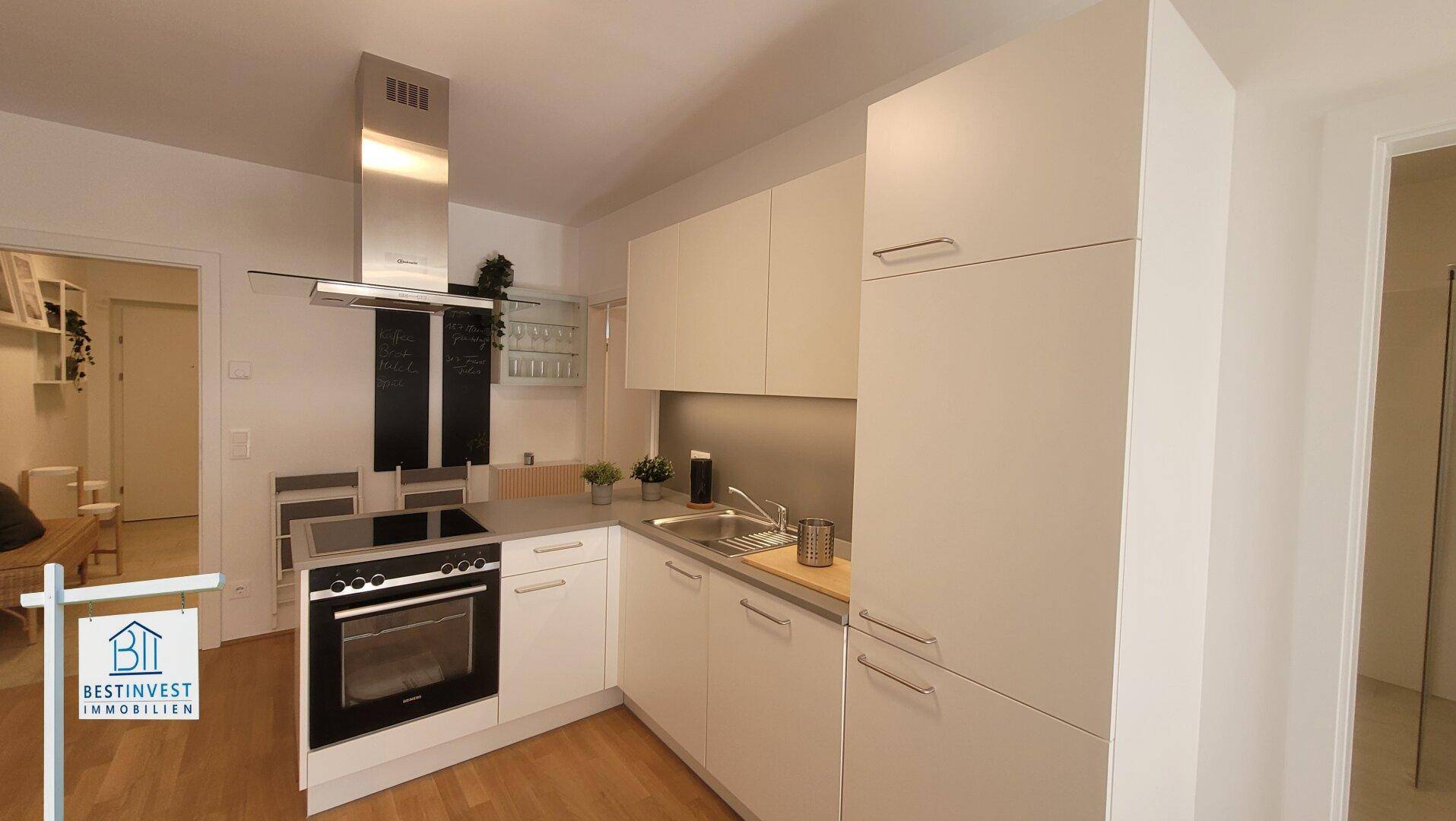 Moderne Einbauküche mit weißen Schränken, Edelstahlgeräten und Dunstabzugshaube.