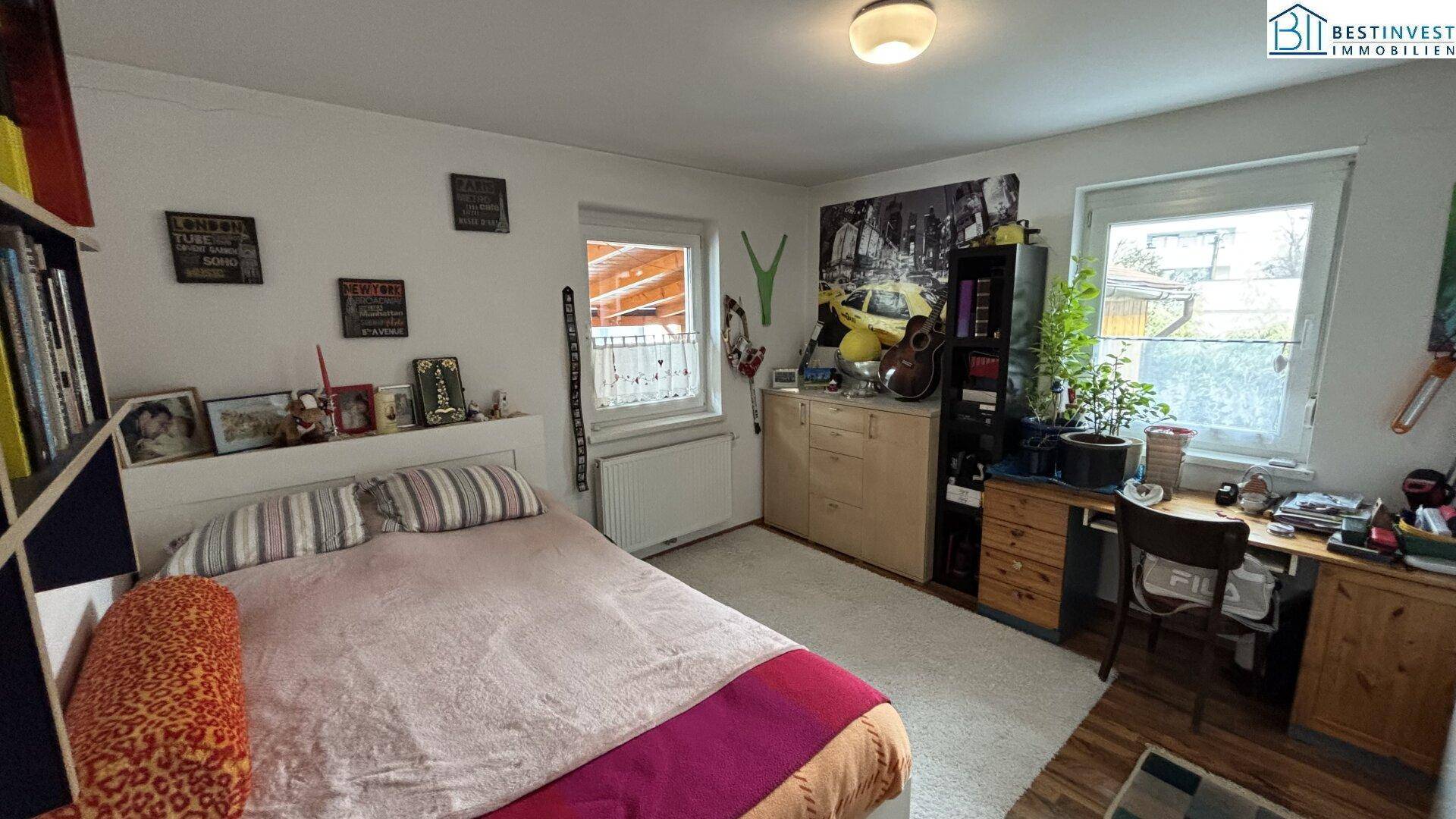 Gemütliches Schlafzimmer mit Teppichboden, großem Bett und Schreibtisch am Fenster.