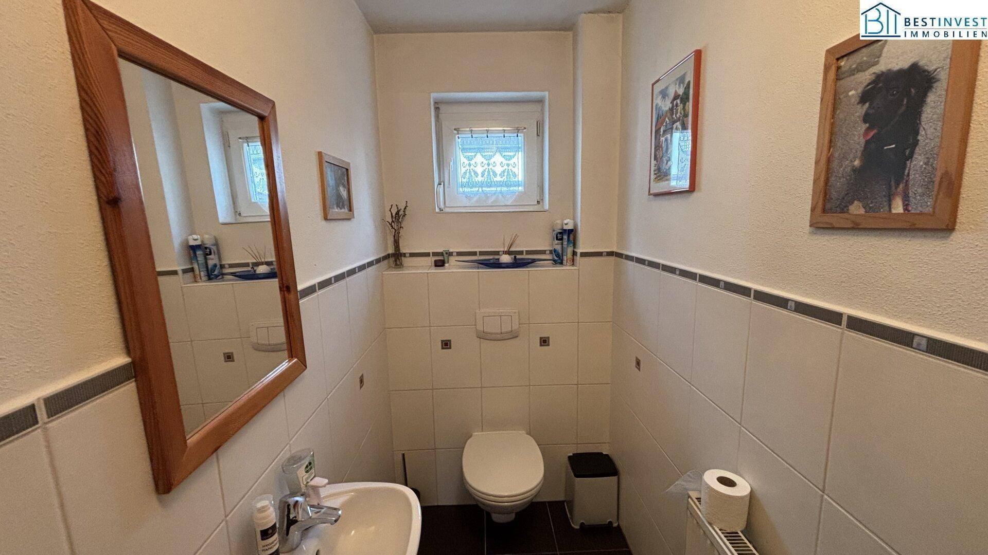 Kleines Gäste-WC mit Fliesenboden, Wand-WC und kleinem Waschbecken.