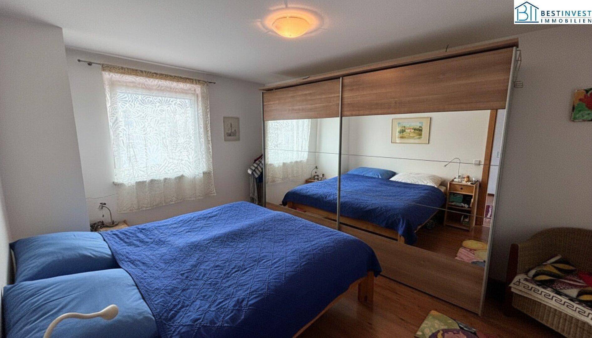 Schlafzimmer mit Doppelbett, Spiegelschrank und Laminatboden, hell und funktional.