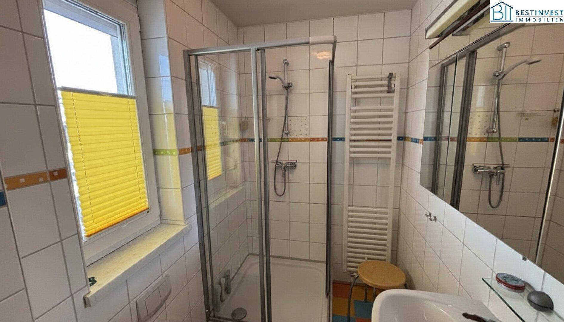 Helles Badezimmer mit Duschkabine, Fliesenboden und beheiztem Handtuchhalter.