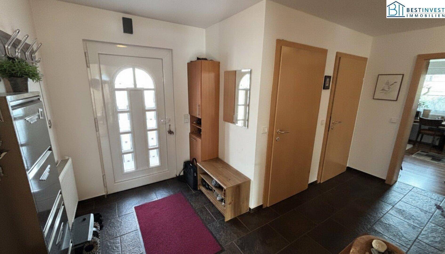 Eingangsbereich mit dunklem Fliesenboden, Garderobe und heller Eingangstür.