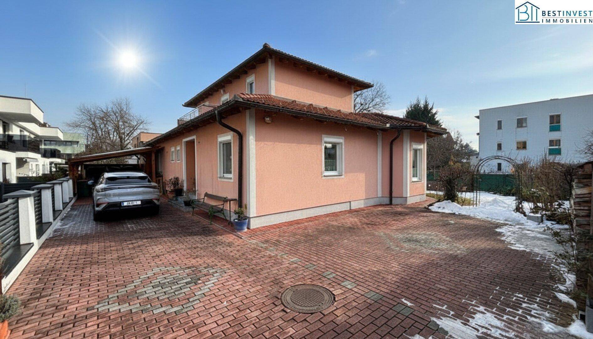 Ansicht des Hauses von der Einfahrt mit gepflastertem Parkplatz und Carport.