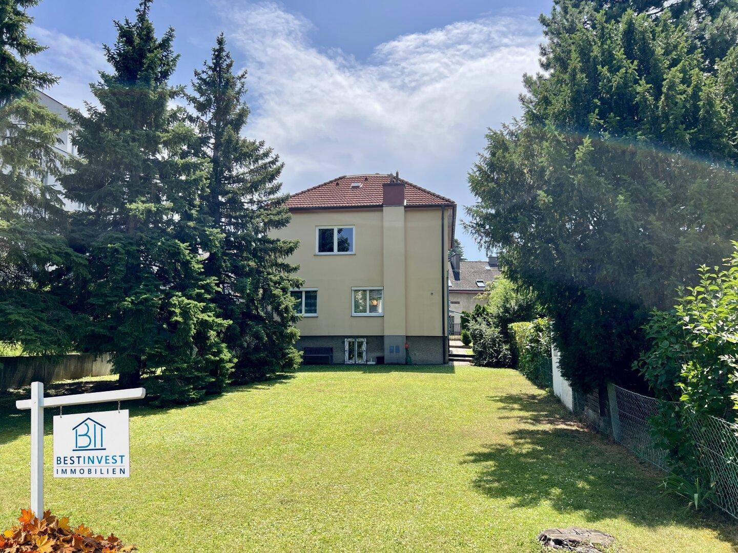 Weitläufiger Garten mit gepflegtem Rasen und hohen Bäumen hinter dem Wohnhaus.