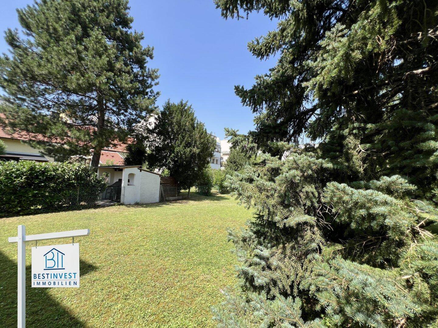 Weitläufiger Gartenbereich mit hohen Bäumen und einem kleinen Gartenhaus im Hintergrund an einem sonnigen Tag.