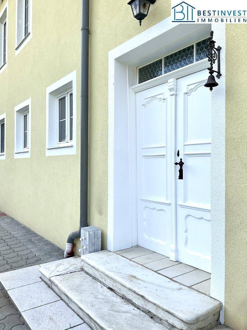 Detailansicht des weißen Haupteingangs mit verzierten Türen, Steinstufen und einer historischen Laterne.