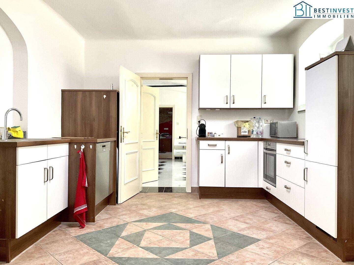Küche mit weißen Schränken, Holzdetails und einem auffälligen Fliesenmuster auf dem Boden.