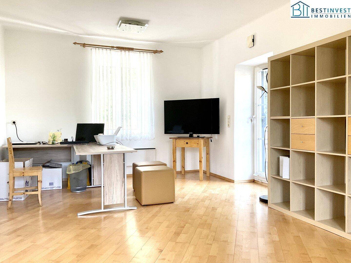 Heller Wohnraum mit Holzfußboden, Schreibtisch und Regalsystem, ideal als Arbeits- und Wohnbereich.