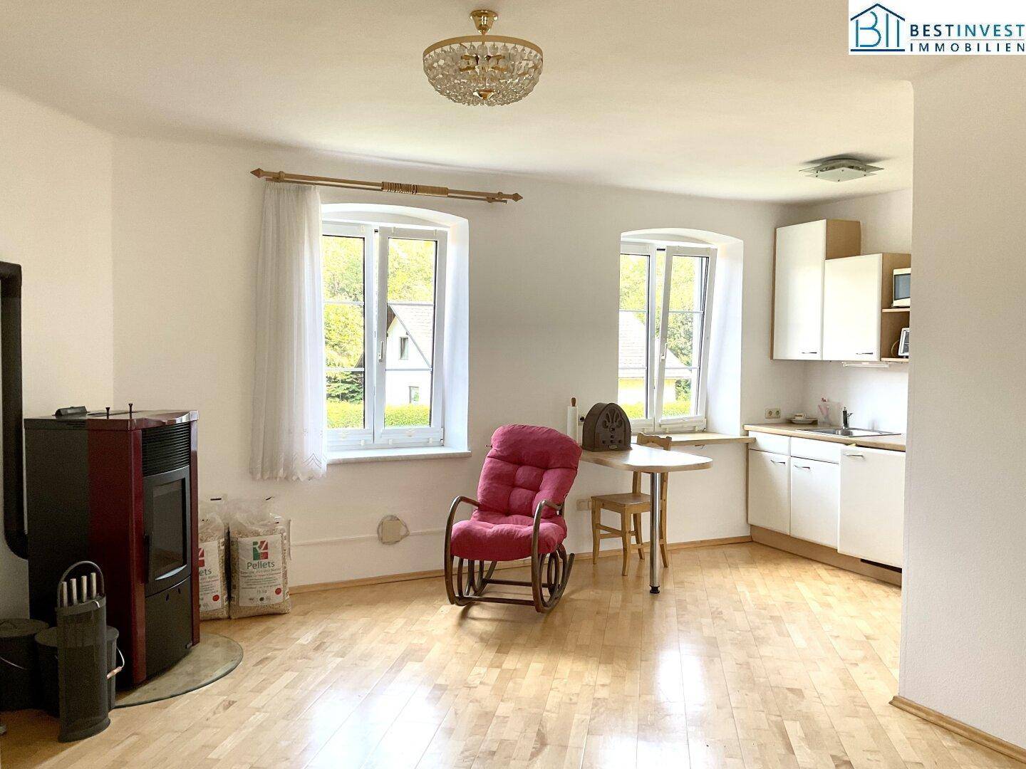 Gemütlicher Wohnbereich mit Holzfußboden, Kaminofen und kleiner Küchenzeile, hell und einladend.