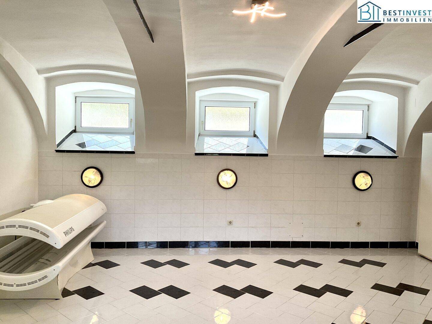 Heller Raum mit gewölbter Decke, drei Fenstern und einem Solarium, geeignet als Wellnessbereich.