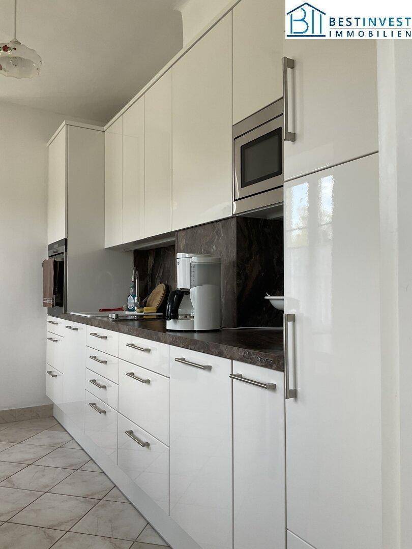 Detailansicht der modernen Küche mit weißen Hochglanzschränken, integrierter Mikrowelle und Kühlschrank.