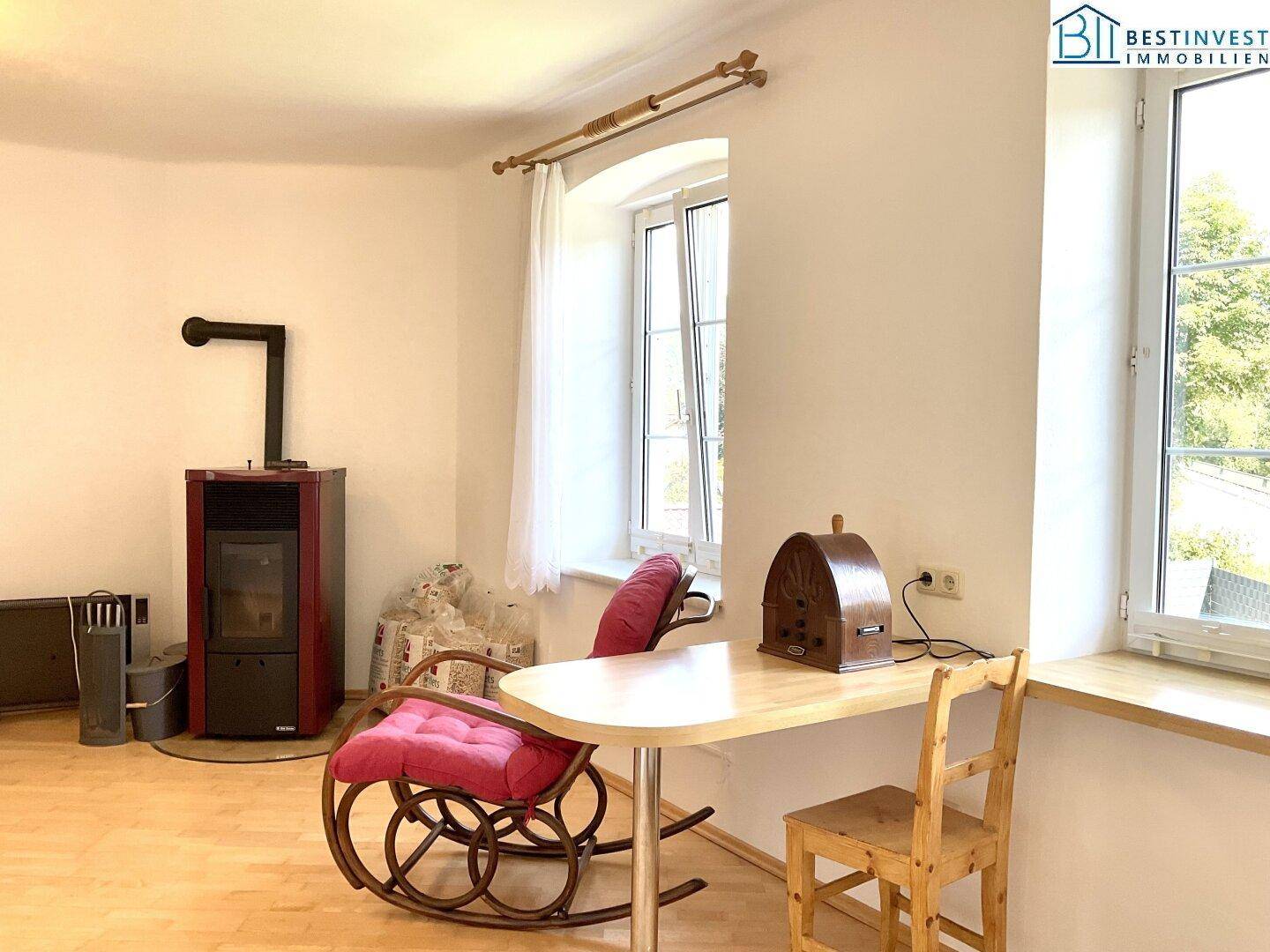 Heller Wohnbereich mit Holzfußboden, Kaminofen und einem Schaukelstuhl, gemütlich und funktional.