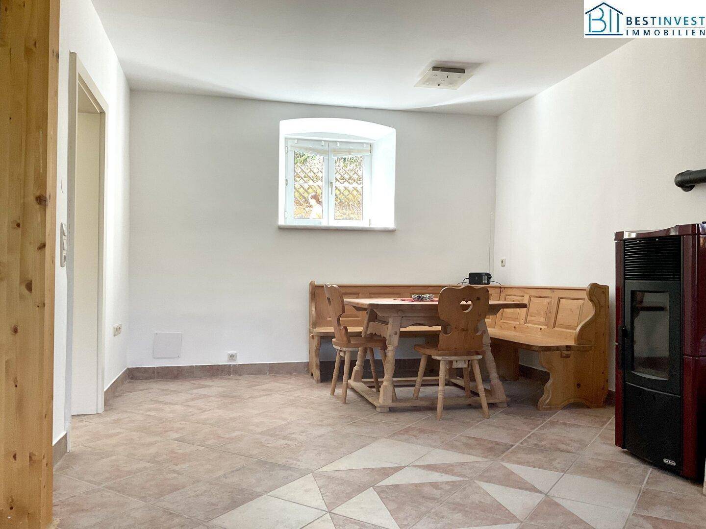 Gemütlicher Essbereich mit Holztisch, Bänken und einem modernen Holzofen, ideal für kalte Tage.