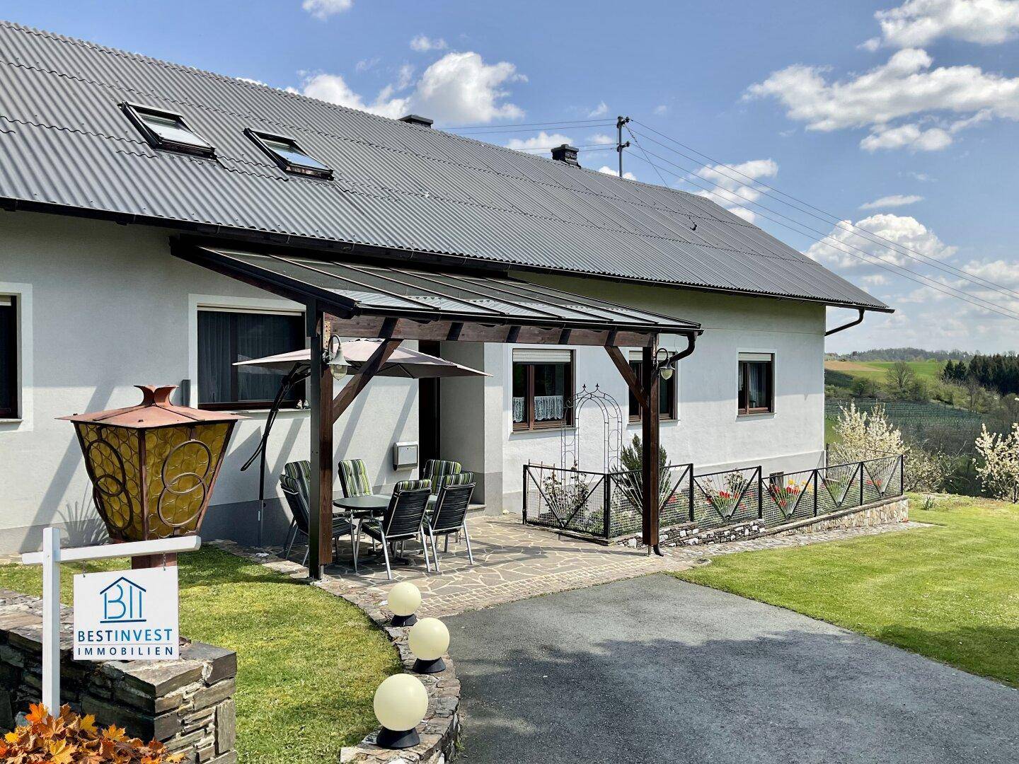 Hausfassade mit einer überdachten Terrasse, die zum Entspannen einlädt, und Blick auf die Landschaft.