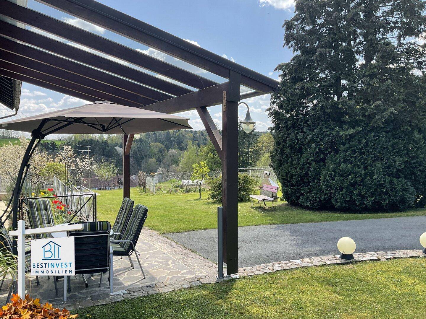 Gemütliche überdachte Terrasse mit Gartenmöbeln und Blick auf den weitläufigen Gartenbereich.