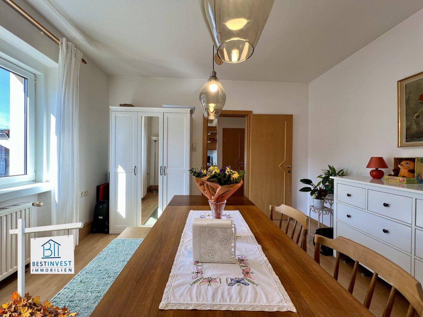Heller Essbereich mit großem Holztisch, modernen Pendelleuchten und weißem Schrank.