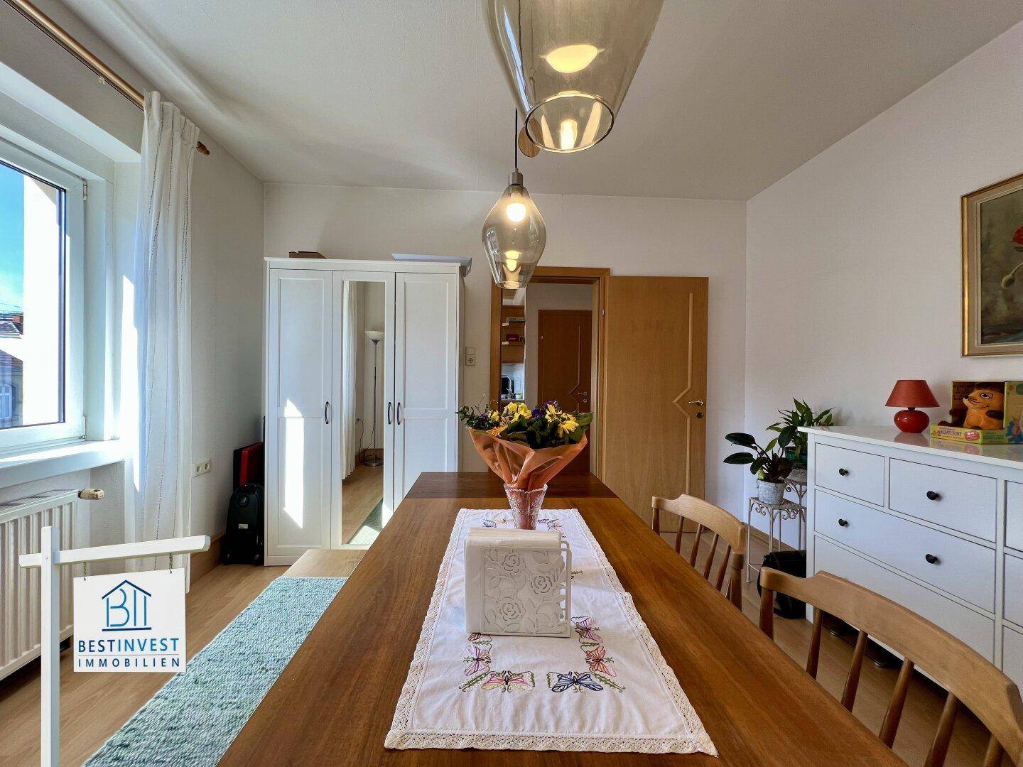 Heller Essbereich mit großem Holztisch, weißem Schrank und Blick nach draußen durch das Fenster.
