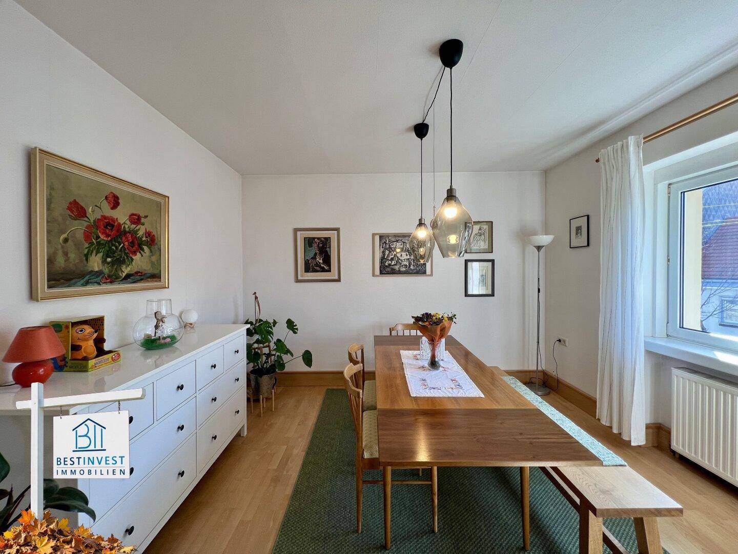 Heller Essbereich mit Holzboden, langer Tafel und Kommode, geschmackvoll dekoriert.
