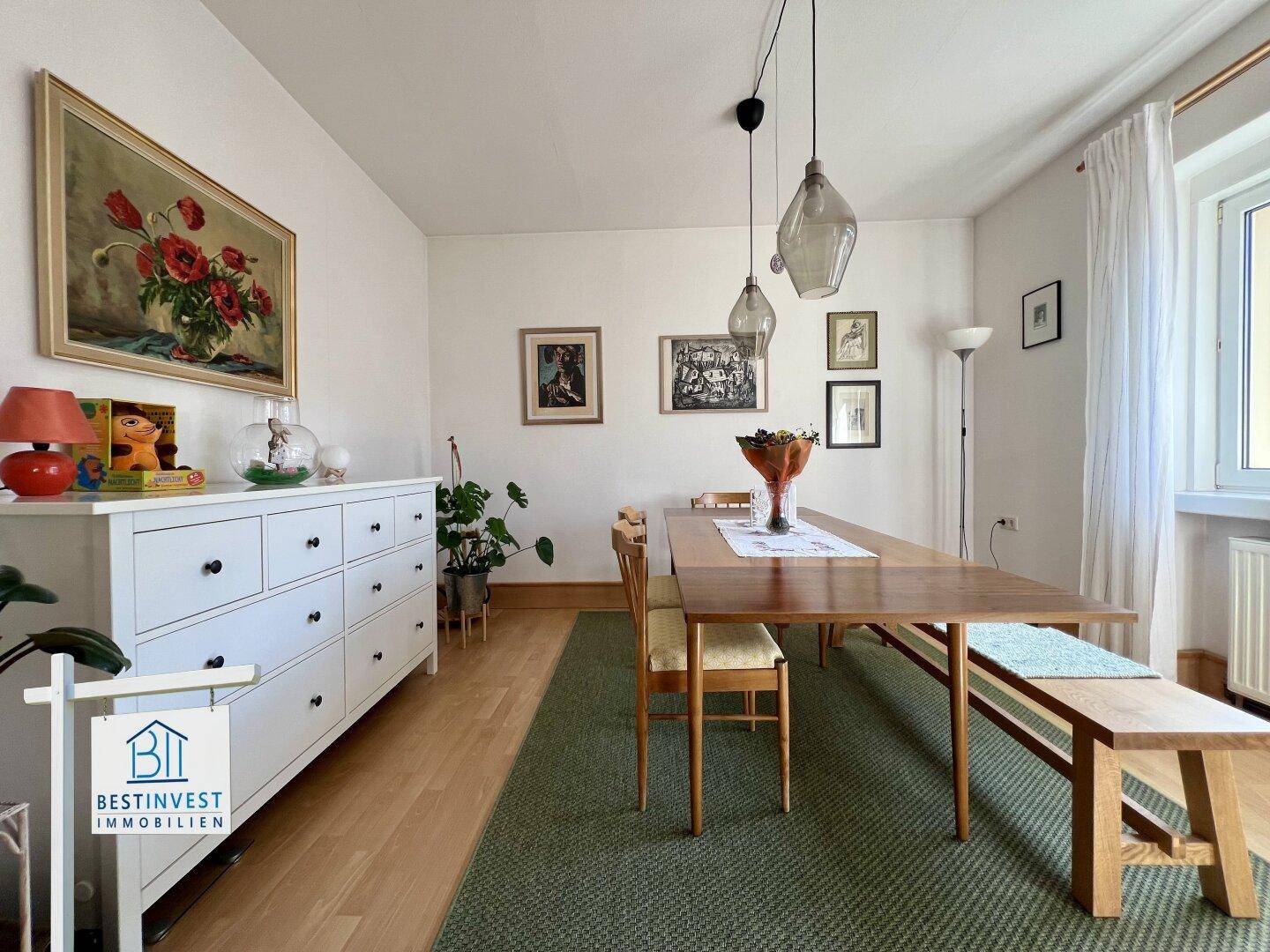 Einladender Essbereich mit Holztisch, Bank und Kommode, umgeben von Kunstwerken an der Wand.