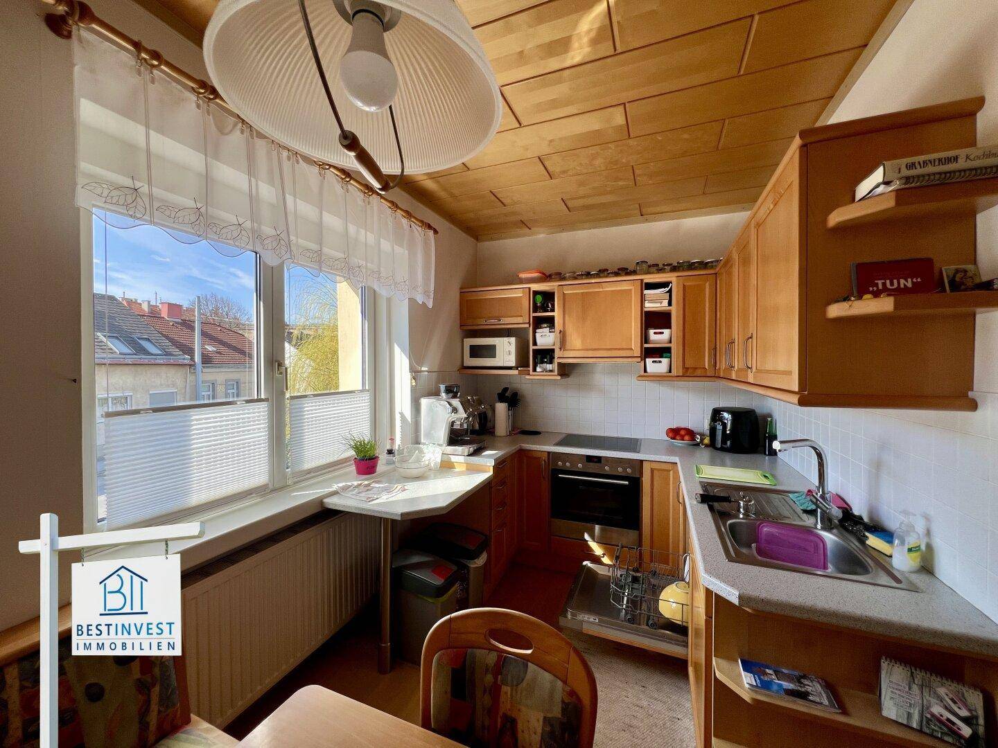Traditionelle Küche mit Holzschränken, Essbereich und Fenster mit Blick ins Grüne.