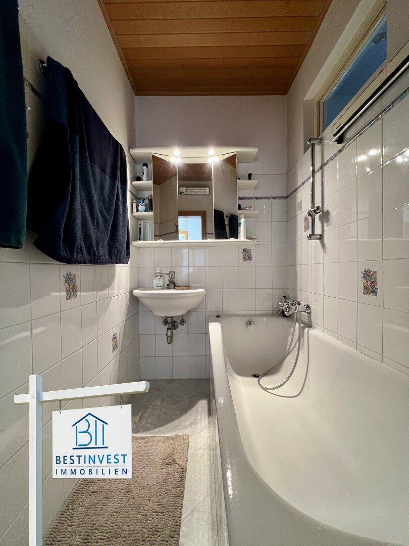 Helles Badezimmer mit Badewanne, Waschbecken und weißen Fliesen in klassischem Stil.