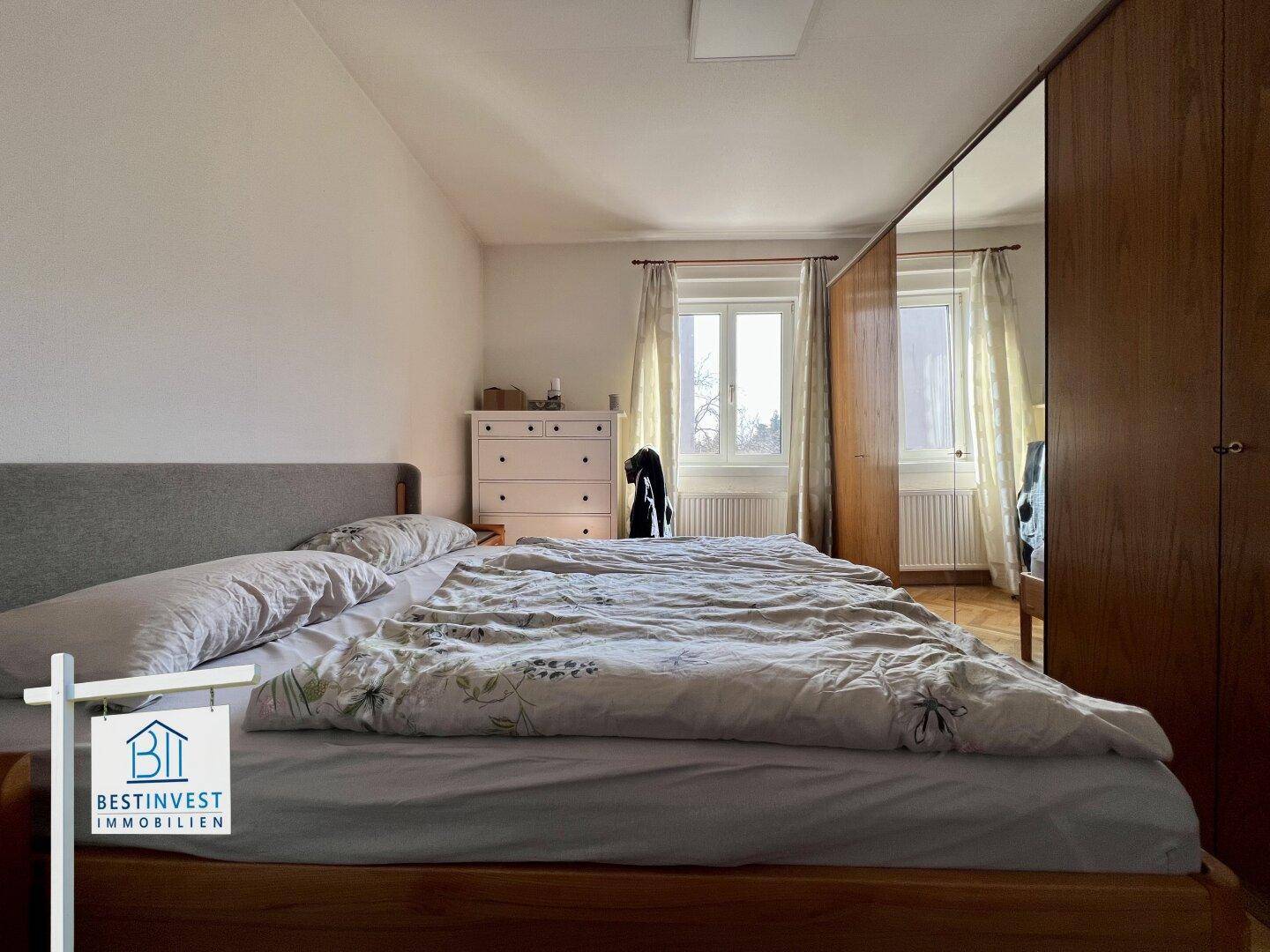 Schlafzimmer mit Doppelbett, Spiegelschrank und Fenster für natürliches Licht.