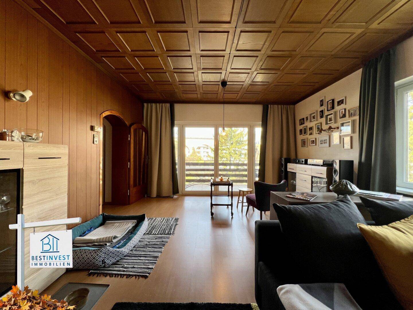 Geräumiges Wohnzimmer mit Holztäfelung an der Decke und Zugang zu einem Balkon.