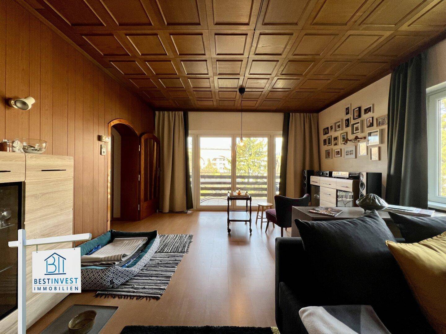 Geräumiges Wohnzimmer mit Holztäfelung an der Decke und Zugang zum Balkon.