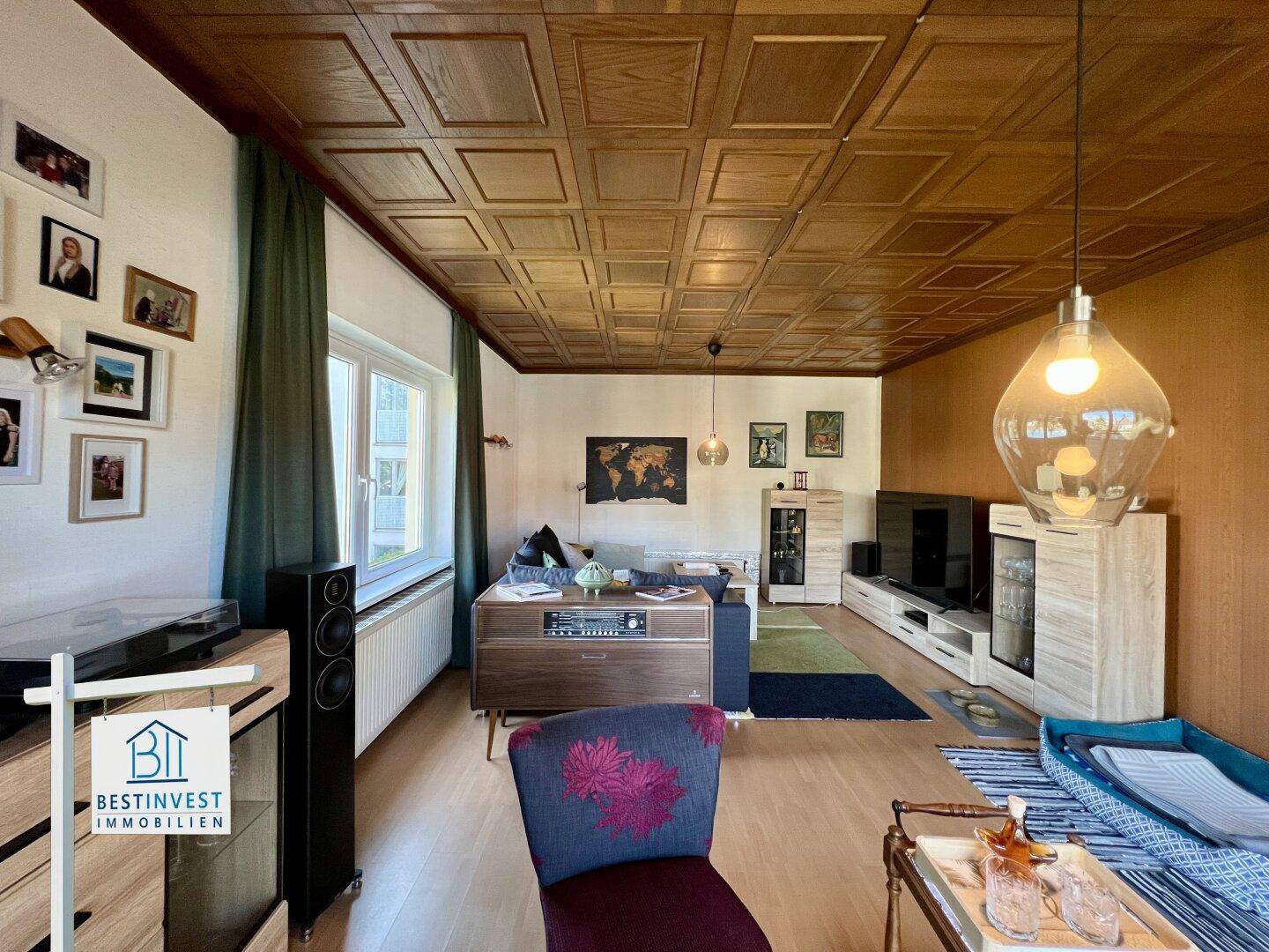 Wohnzimmer mit Holztäfelung, großem Fenster und Blick auf den Außenbereich.