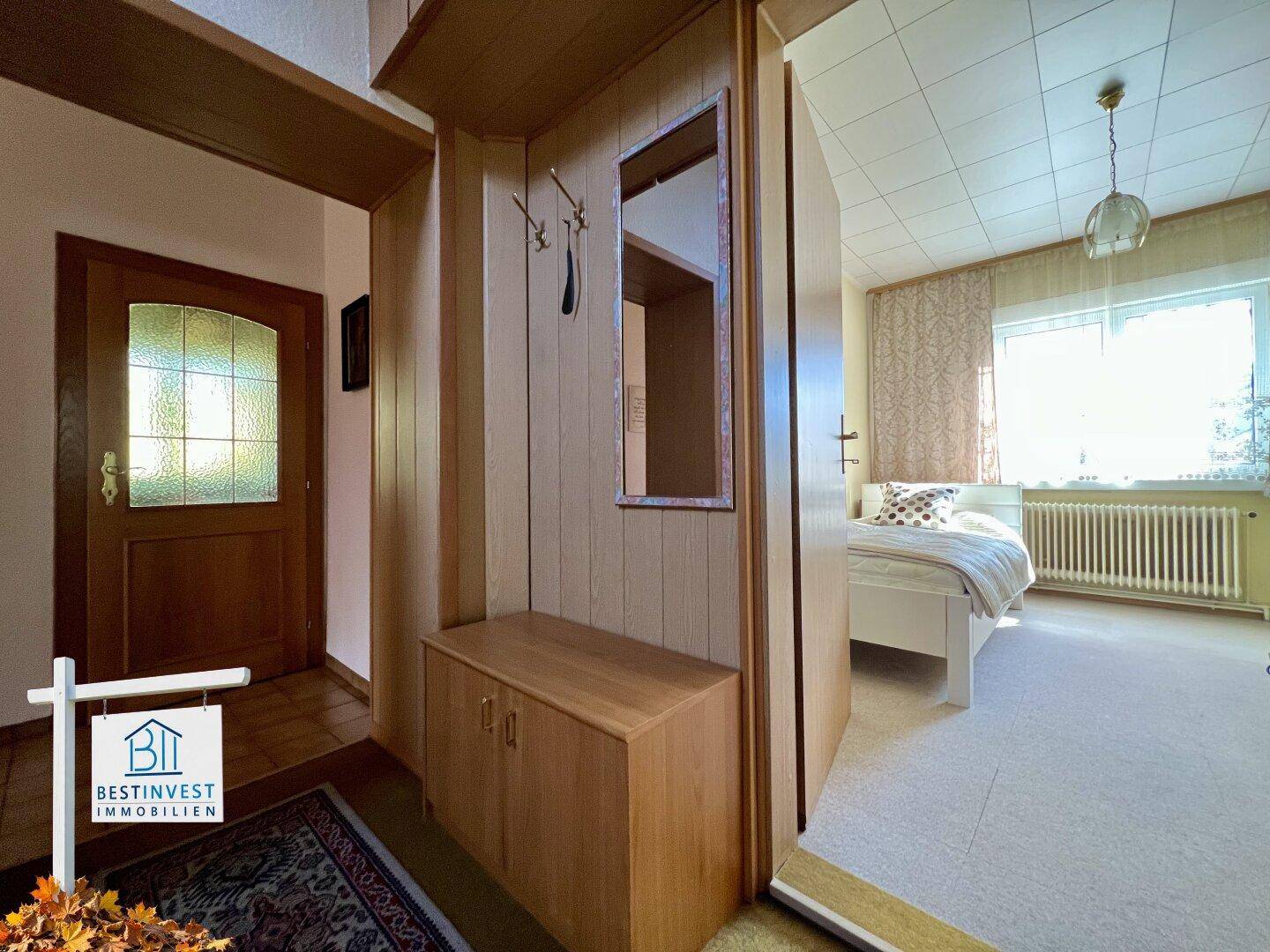 Eingangsbereich mit Garderobe und Spiegel, der zu einem Schlafzimmer führt.