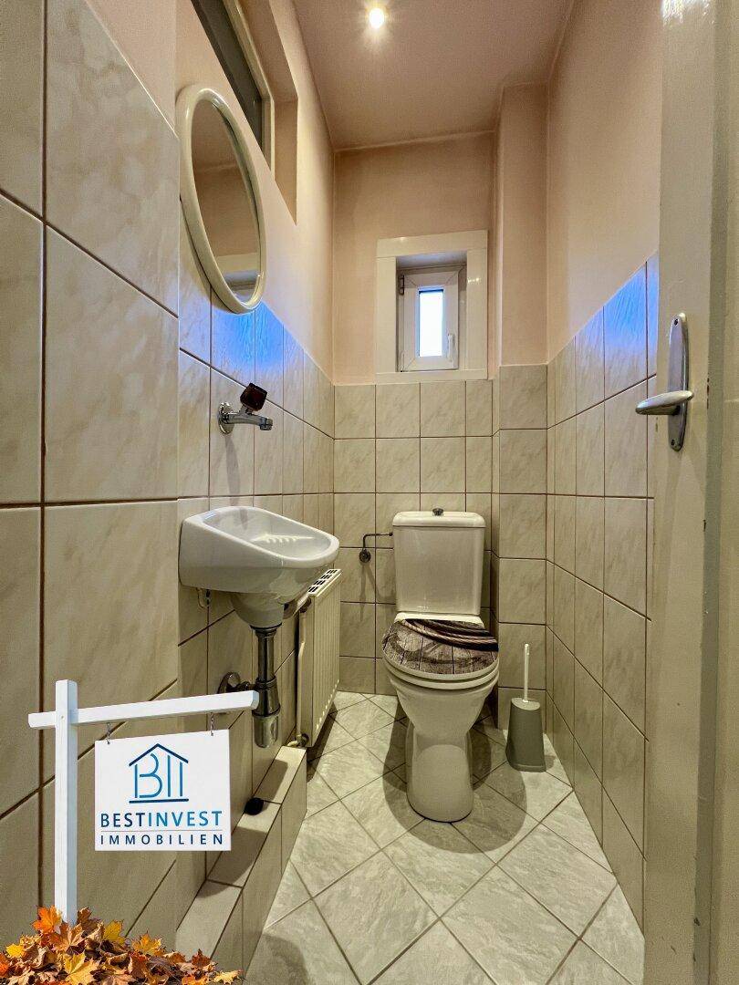 Kleines Gäste-WC mit Fliesenboden, Wand-WC und kleinem Waschbecken.
