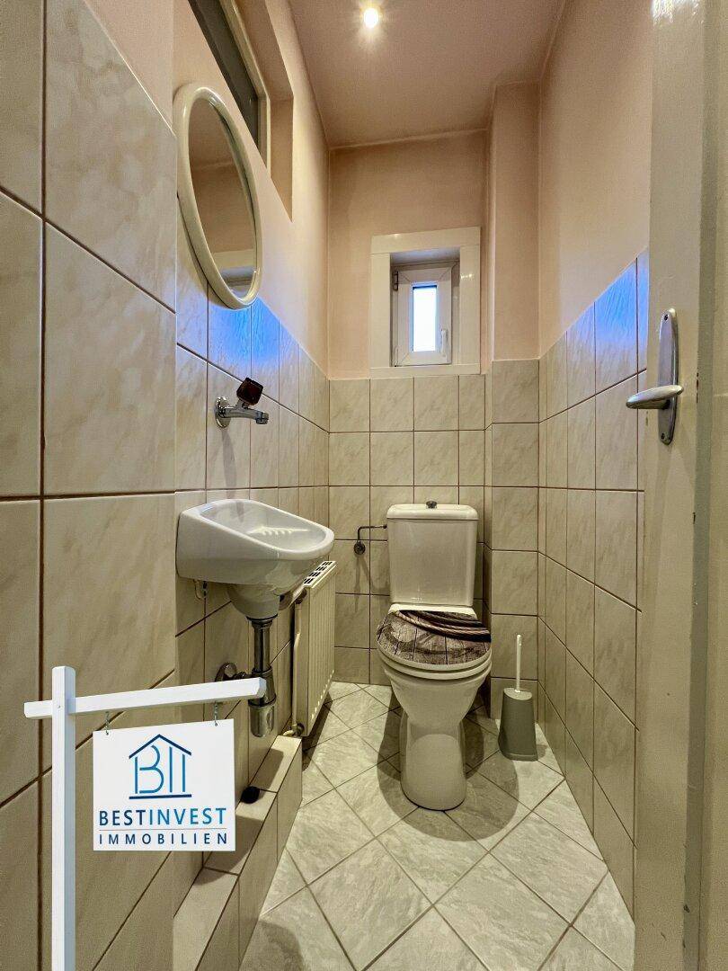 Kleines Gäste-WC mit Waschbecken, Toilette und Fliesen in Pastellfarben.