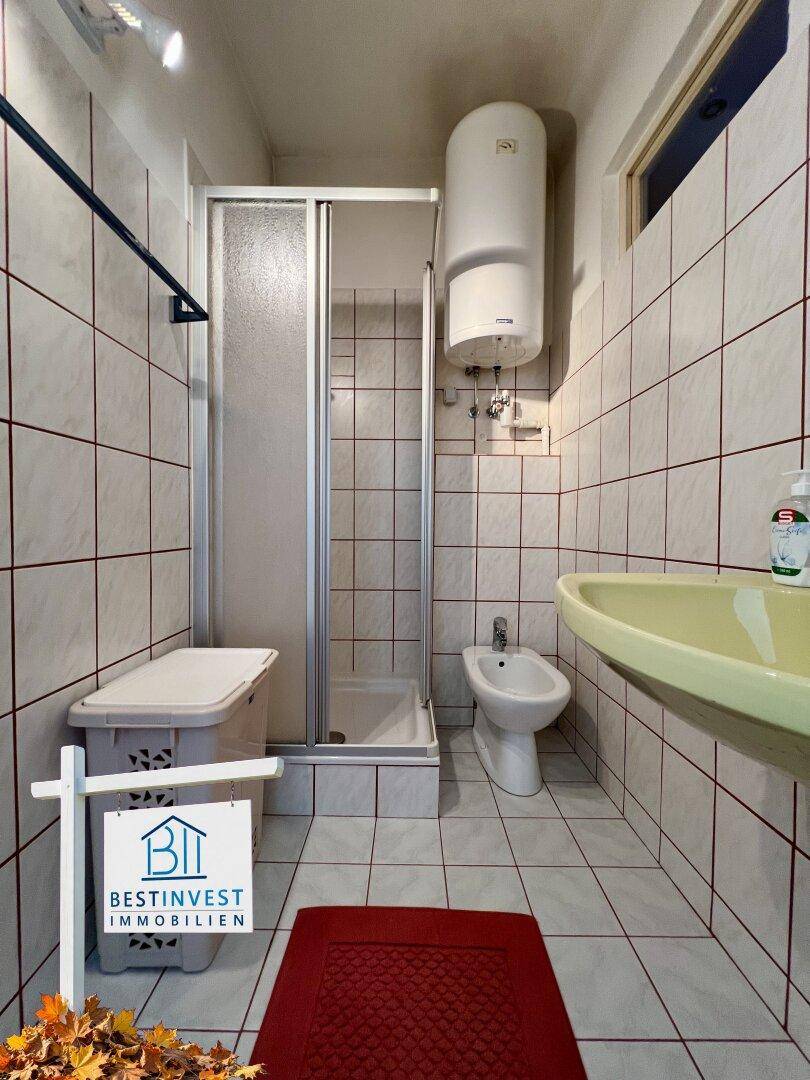 Badezimmer mit Duschkabine, Bidet und Waschbecken, komplett gefliest.