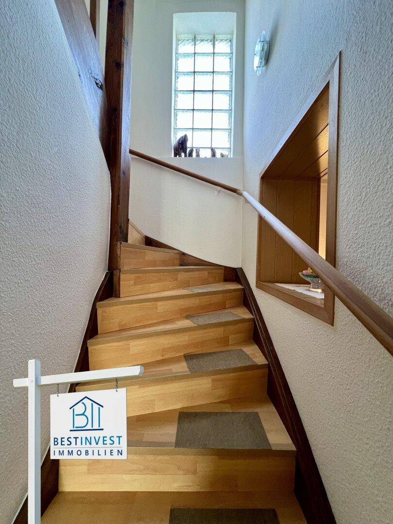 Holztreppe mit Geländer und einem Fenster aus Glasbausteinen für natürliches Licht.