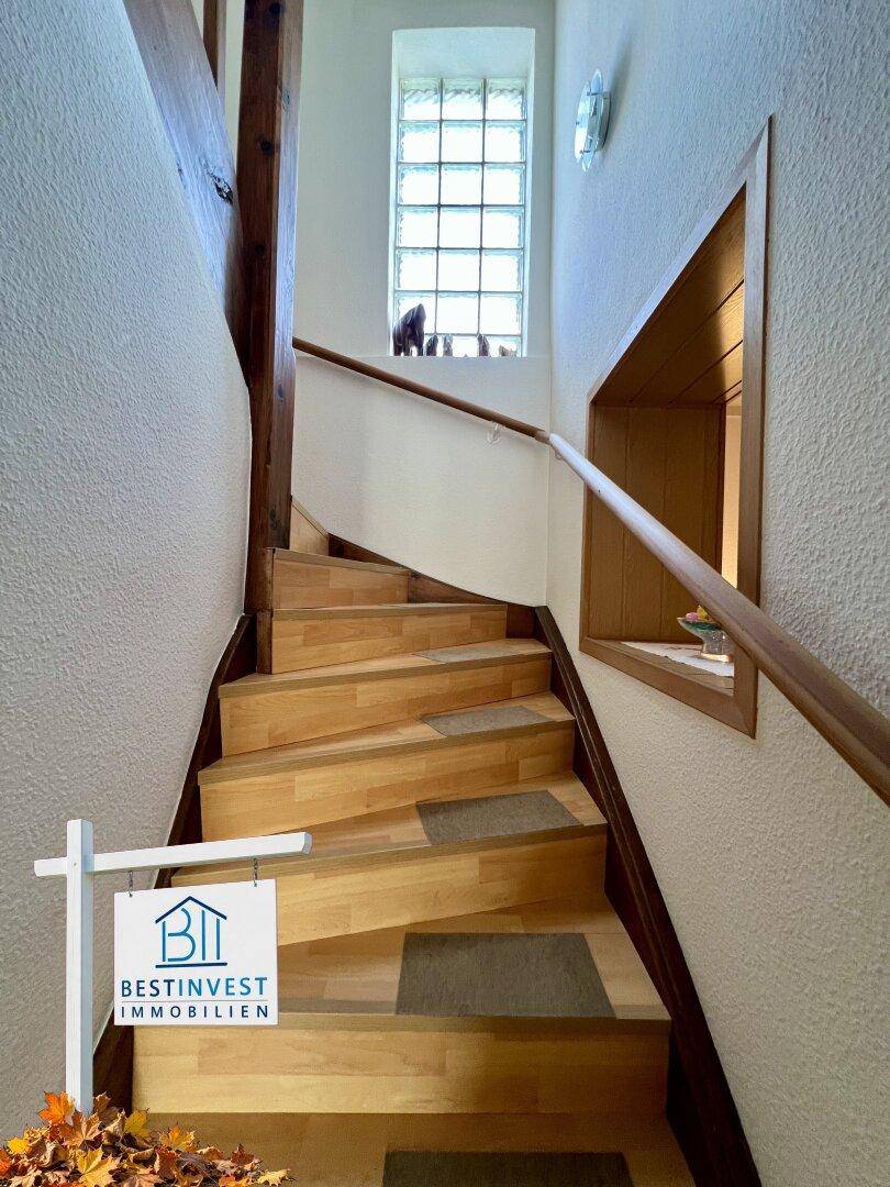 Holztreppe mit Geländer und einem Fenster aus Glasbausteinen für natürliches Licht.