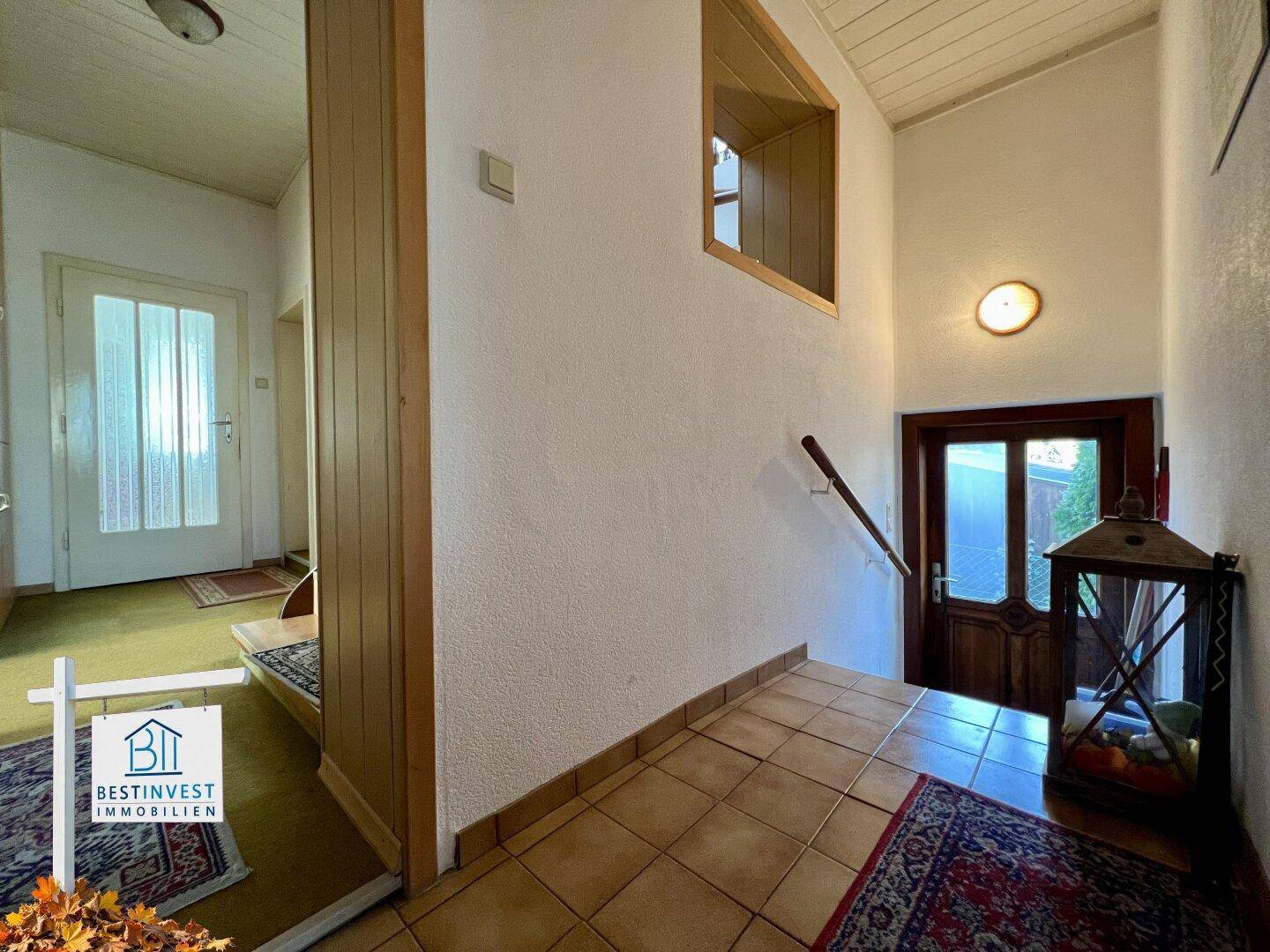Eingangsbereich mit Fliesenboden, Holztür und Zugang zum Treppenhaus.
