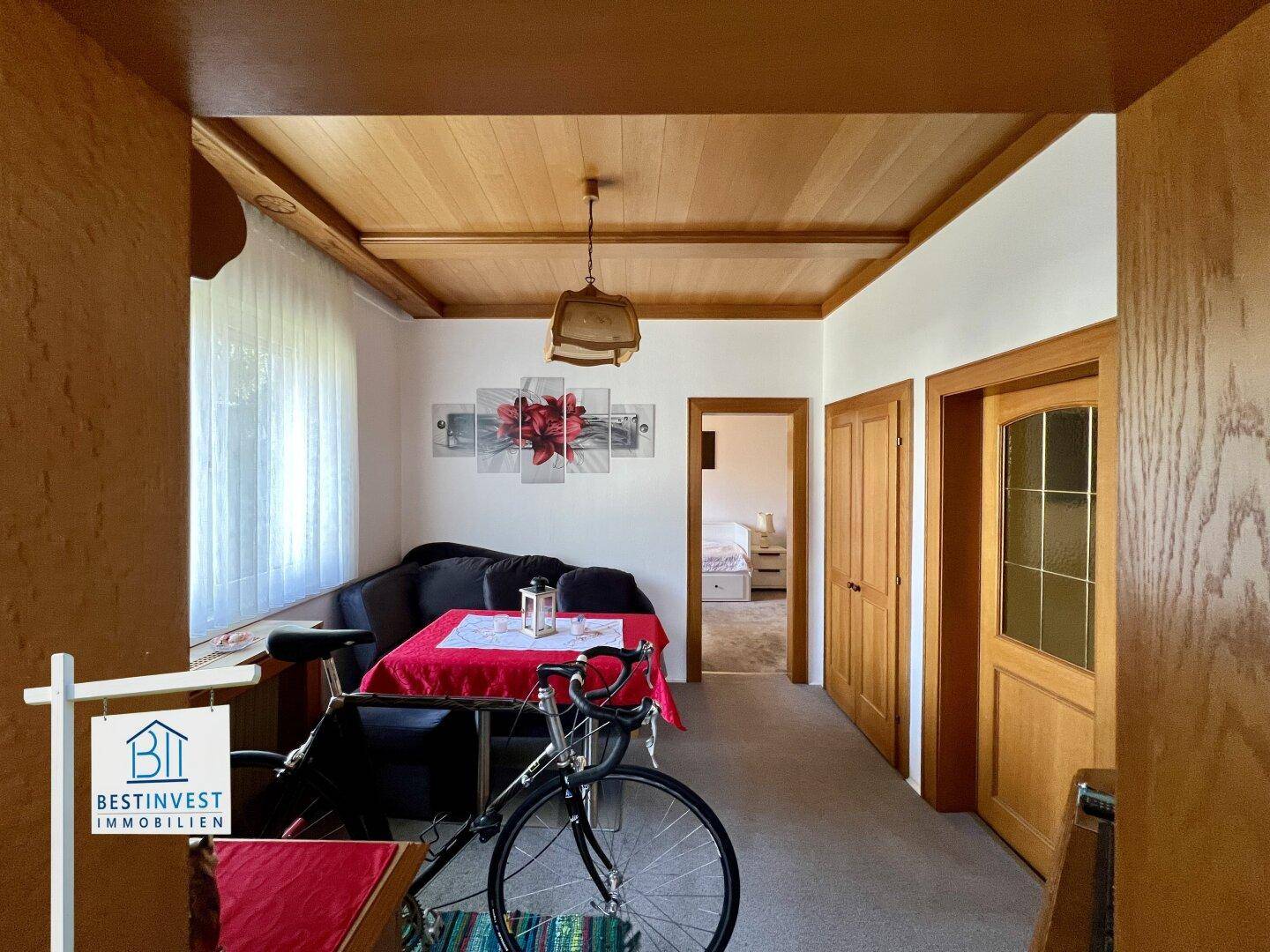 Multifunktionaler Raum mit Holztäfelung, Sofa und Essbereich, verbunden mit einem weiteren Zimmer.
