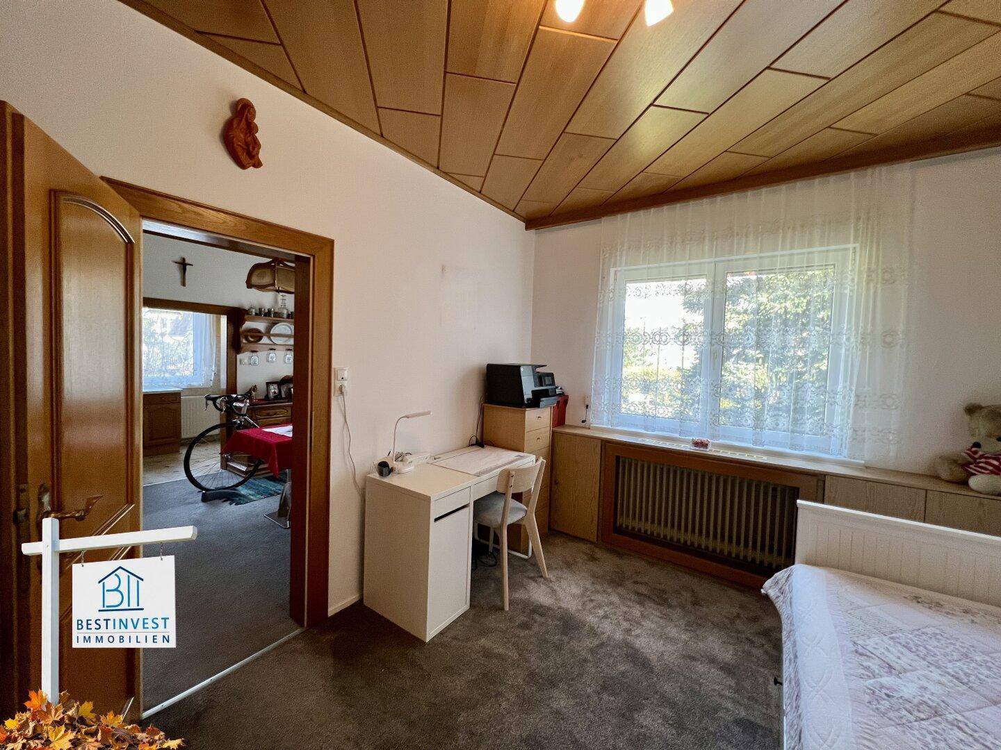Helles Arbeitszimmer mit Schreibtisch, Einzelbett und Fenster mit Blick ins Grüne.